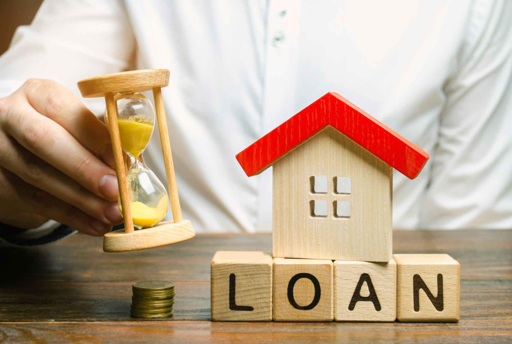 Wooden blocks with the word Loan, miniature house and hourglass in the hands of a businessman